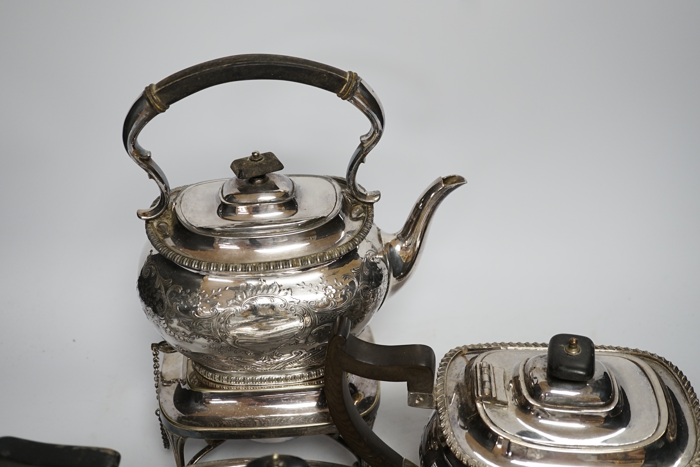 A plated kettle on stand, two plated teapots, a sugar bowl and a cream jug